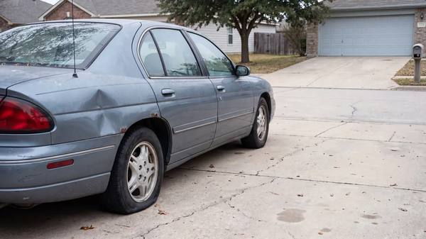 An older sedan with a dented rear quarter panel parked on a residential concrete driveway