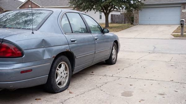 An older sedan with a dented rear quarter panel parked on a residential concrete driveway
